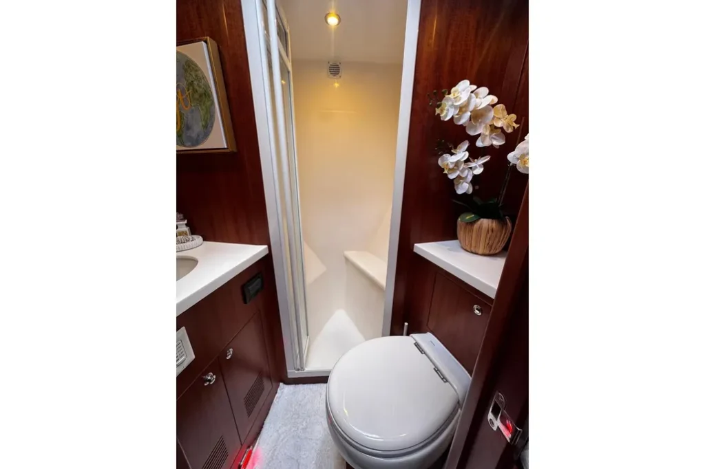 2025 Nordhavn 475 Listo guest head with separate glass shower stall, marine toilet, and built-in mahogany cabinetry