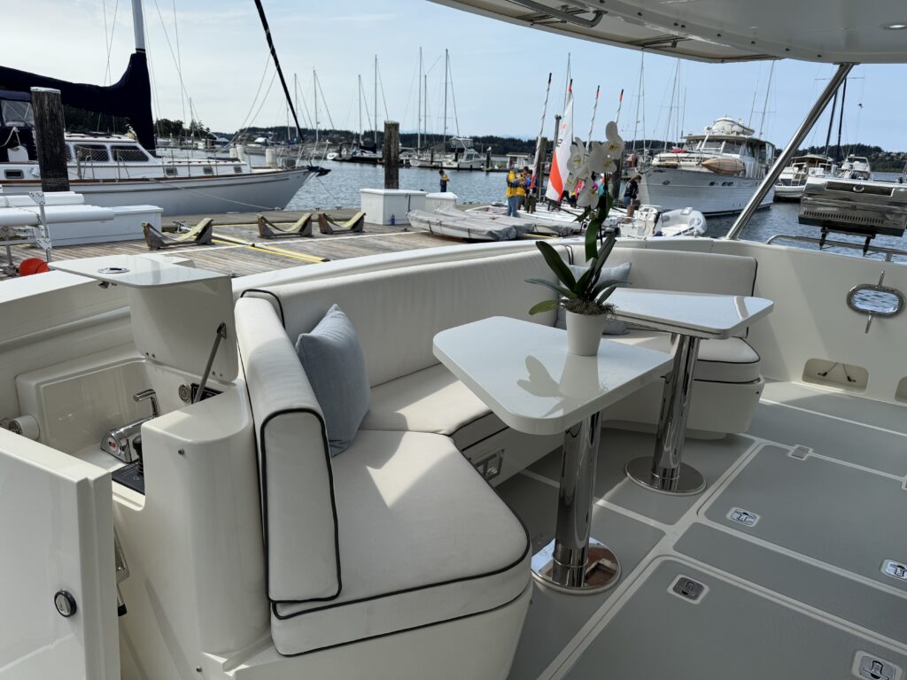 N6416 - AEGEAN MIST - aft cockpit lounge with white settee cushions, pedestal dining table with orchid centerpiece, and busy marina with sailboats in the background