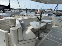 N6416 - AEGEAN MIST - aft cockpit lounge with white settee cushions, pedestal dining table with orchid centerpiece, and busy marina with sailboats in the background
