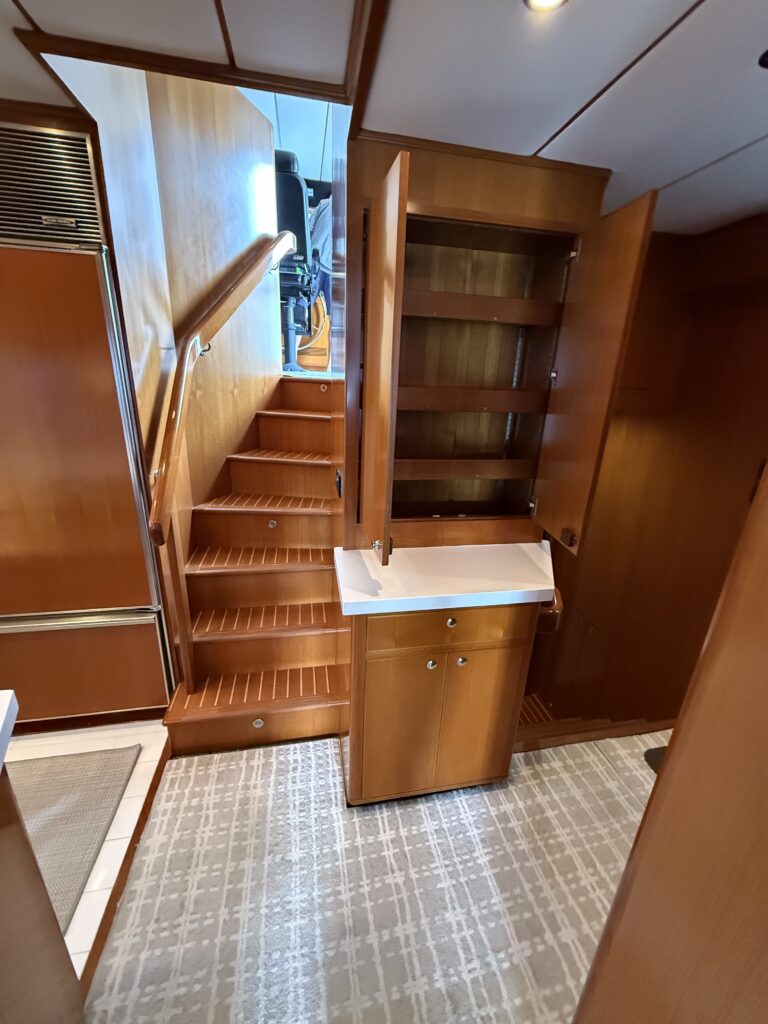 N6416 - AEGEAN MIST - interior staircase leading to pilothouse with open teak cabinetry, small vanity shelf, and cabin doorway visible