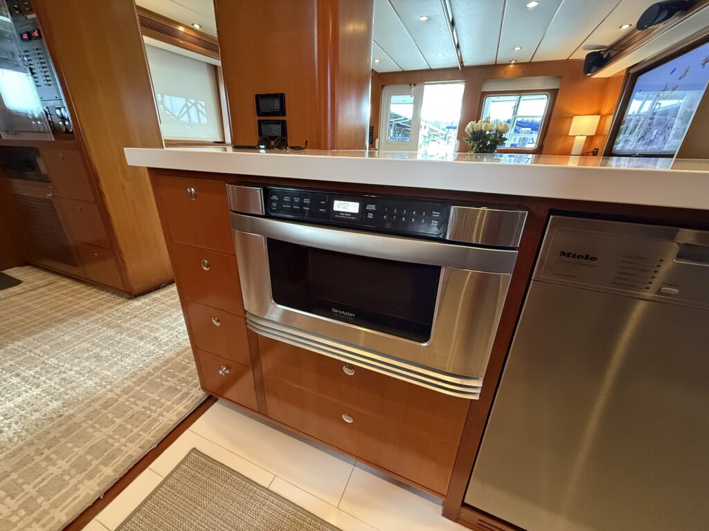 N6416 - AEGEAN MIST - galley island viewed from above showing white quartz countertop, undermount stainless sink, and open pass-through view to salon with orchid and roses