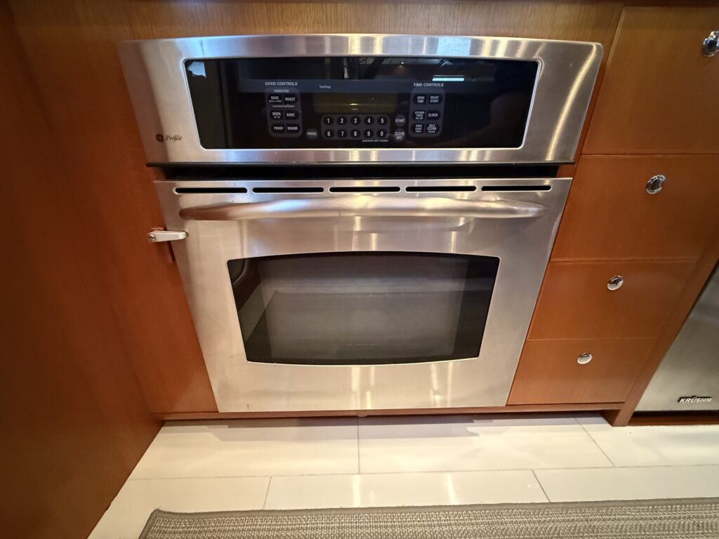 N6416 - AEGEAN MIST - full galley view showing induction cooktop, wall oven, undercounter refrigerator, sink, subway tile backsplash, and porthole access door to exterior