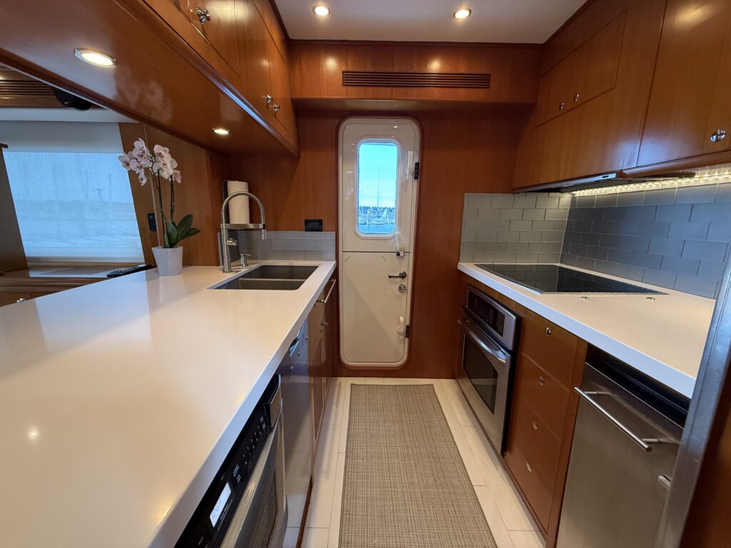 N6416 - AEGEAN MIST - pilothouse interior with two black leather captain's chairs, stainless helm wheel, navigation electronics at console, and panoramic windows overlooking marina