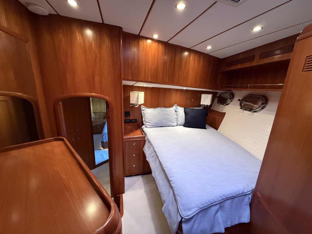 N6416 - AEGEAN MIST - master stateroom with queen bed dressed in white linens and navy accent pillow, teak bulkheads, brass porthole, vanity mirror, and reading lamps