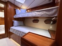 N6416 - AEGEAN MIST - guest stateroom with two bunk berths dressed in light blue linen, brass oval portholes, teak woodwork, built-in drawers, and reading light