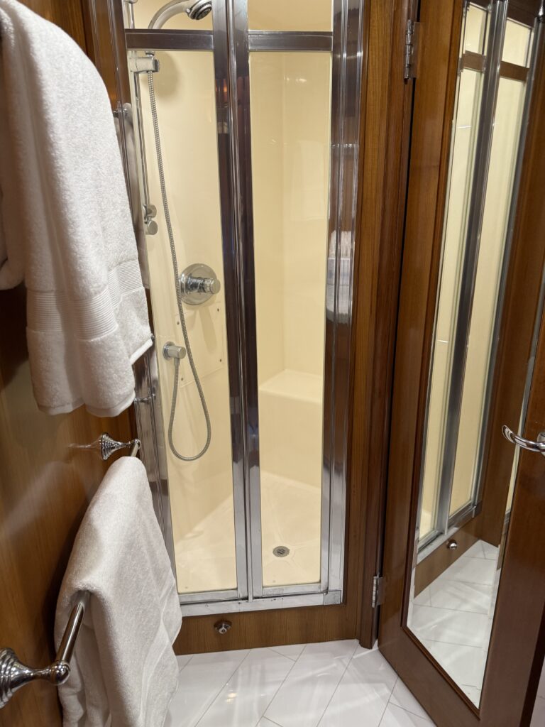 N6416 - AEGEAN MIST - master head glass shower enclosure with stainless trim, hand shower, and folded white towels on teak vanity ledge