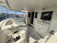 N6416 - AEGEAN MIST - aft cockpit deck with helm station, white leather seating, stainless ladder to flybridge, and marina with other vessels visible in the background