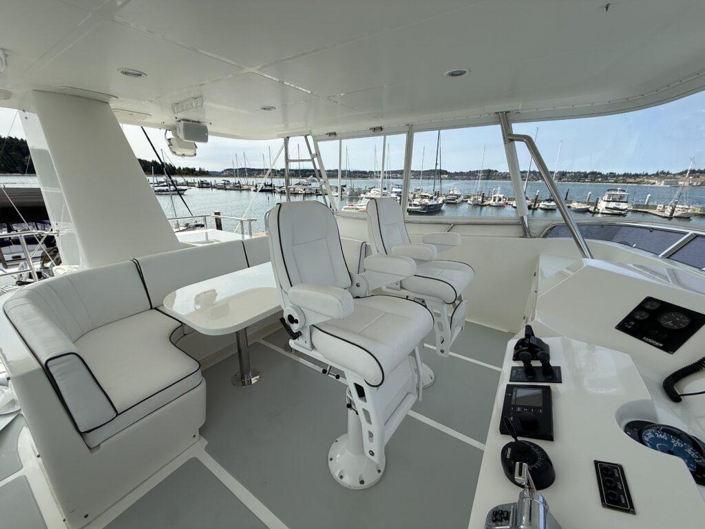 N6416 - AEGEAN MIST - flybridge with two white pedestal captain's chairs, port-side white settee with table, helm instruments, and open water marina views all around