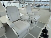N6416 - AEGEAN MIST - close-up of two white leather flybridge captain's chairs with black accent piping facing forward toward the marina