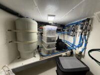 N6416 - AEGEAN MIST - below-decks water system compartment with grey pressure tank, water manifolds, blue hoses, and storage bins