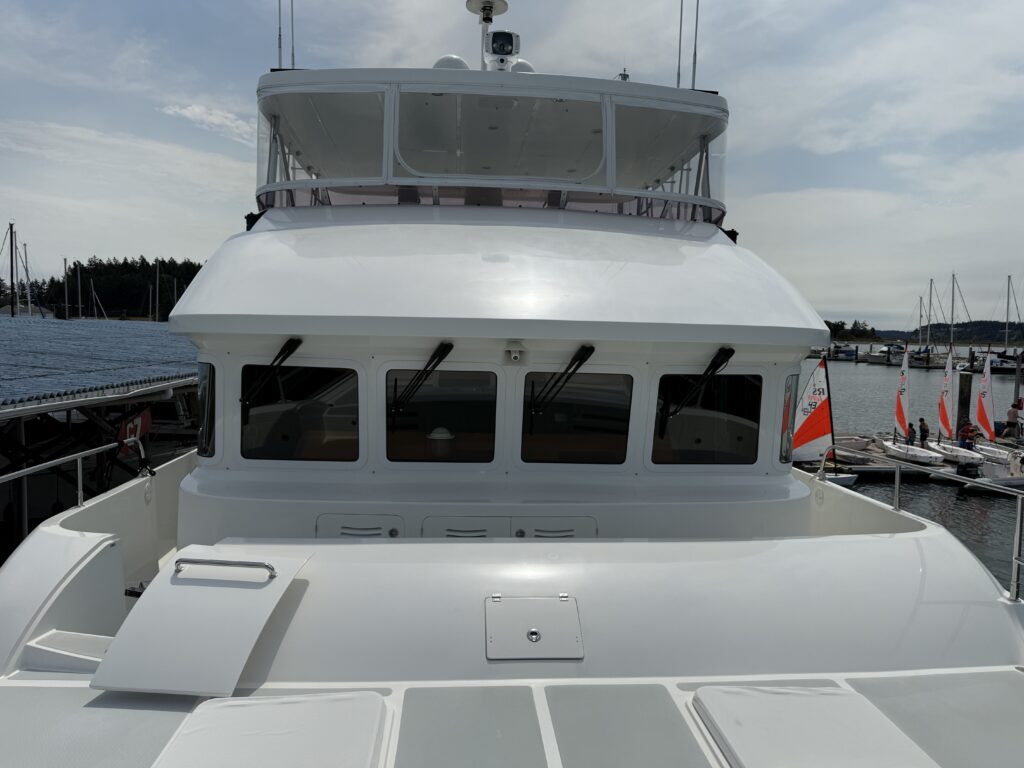 N6416 - AEGEAN MIST - bow-on view of white Nordhavn trawler at dock showing pilothouse windows, radar arch, foredeck hatches, and marina with sailboats in background
